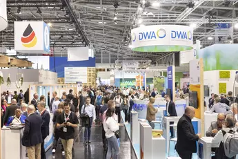 Geschäftiges Treiben auf der Weltleitmesse IFAT Munich. Zahlreiche Besucher informieren sich an den Messeständen und nutzen die Gelegenheit zum Networking. Über den Ständen sind Schilder von Ausstellern wie DWA und anderen Unternehmen der Umweltbranche zu sehen.