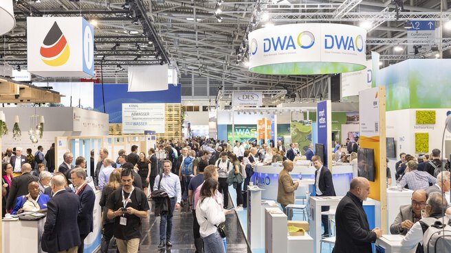 Busy atmosphere at the world’s leading trade fair IFAT Munich. Numerous visitors gather information at the exhibition stands and take the opportunity to network. Signs from exhibitors such as DWA and other companies from the environmental sector can be seen above the stands.