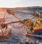 A huge mining excavator loads stones into a dump truck at sunset.