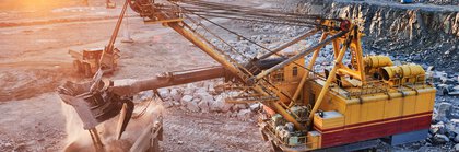 A huge mining excavator loads stones into a dump truck at sunset.