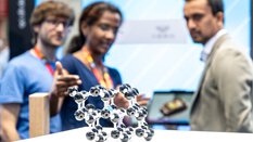 Close-up of a molecule model. In the background, three people discussing can be seen out of focus.
