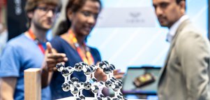 Close-up of a molecule model. In the background, three people discussing can be seen out of focus.