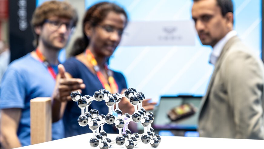 Close-up of a molecule model. In the background, three people discussing can be seen out of focus.