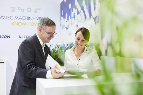 Two professionals smile and review documents at a bright, modern office desk decorated with green plants.