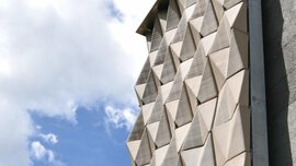 Modern building facade with geometric, angular panels against a blue sky with scattered white clouds.