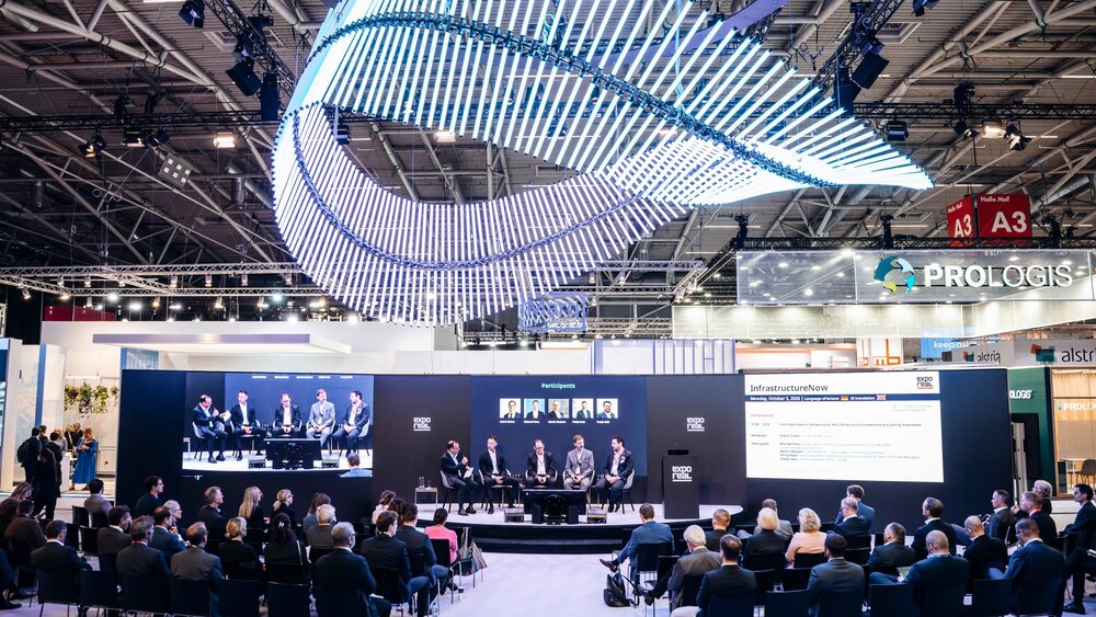 Panel discussion on a stage in front of a seated audience in an exhibition hall.
