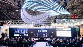Panel discussion on a stage in front of a seated audience in an exhibition hall.