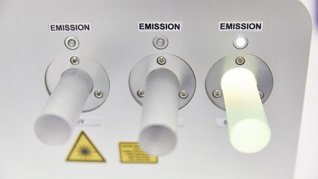 Laseremitter mit 3 Ausgängen in denen zylindrische Diffusoren stecken, einer davon ist hell erleuchtet.