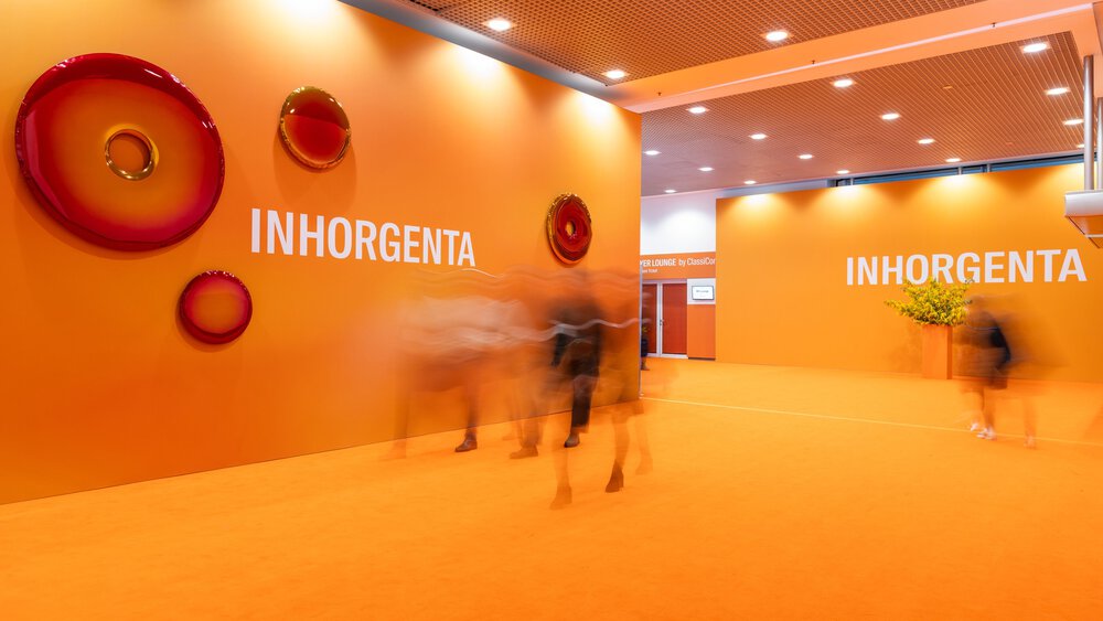 Man geht durch einen orangefarbenen Flur mit der Aufschrift INHORGENTA an der Wand und kreisförmiger Wandkunst.