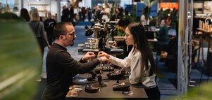 Two people are standing at a table at INHORGENTA trying on jewelry.
