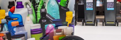 Various colorful plastic bottles with recycling containers in the background.
