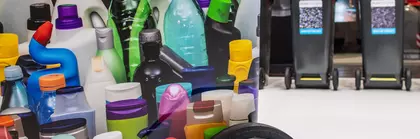 Various colorful plastic bottles with recycling containers in the background.