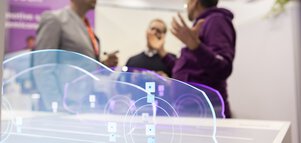 Drei Personen diskutieren an einem Messestand. Im Vordergrund sind drei beleuchtete, aus Plexiglas geschnittene Silhouetten von Autos ausgestellt.