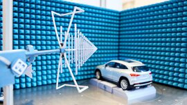 Ein Stand auf der productronica Messe mit gepolsterten hellblauen Wänden, einem weißen Kleinwagen auf einer Art Plattform und einer Vorrichtung mit weißen Streben.