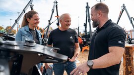 Ein Mitarbeiter zeigt zwei Besuchern die Bauteile einer Forstmaschine und erklärt ihnen das Gerät.