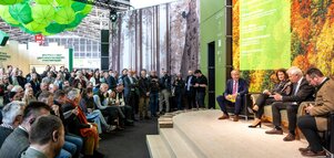 Three people sit on stage during a panel discussion in front of a large audience.