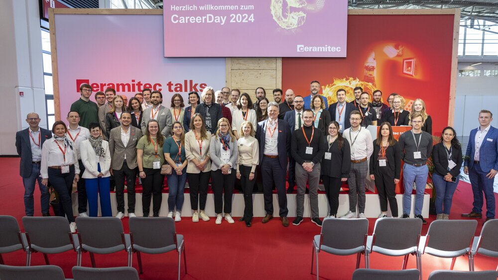 A large group of people stand on and around a stage for a group photo. Above them hangs a screen displaying the words “CareerDay 2024”.