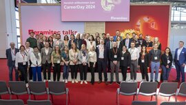 A large group of people stand on and around a stage for a group photo. Above them hangs a screen displaying the words “CareerDay 2024”.