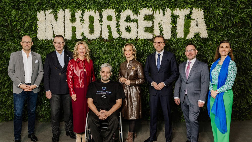 Eight people stand smiling in front of a green wall of plants with the word INHORGENTA spelled out in white flowers.