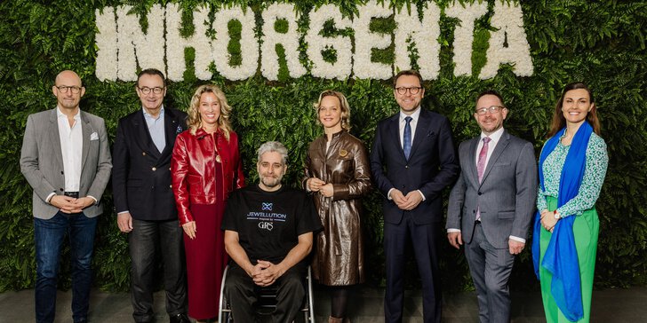 Eight people stand smiling in front of a green wall of plants with the word INHORGENTA spelled out in white flowers.