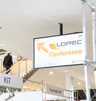 Sign for the LOPEC conference next to an escalator in a modern building.