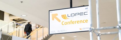 Sign for the LOPEC conference next to an escalator in a modern building.