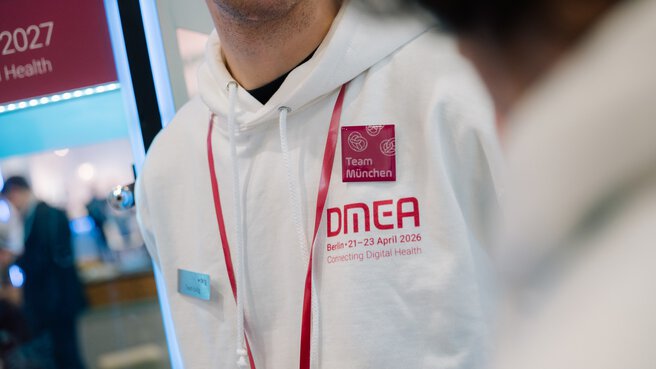 Staff member wearing a white DMEA hoodie with Team Munich badge and event lanyard