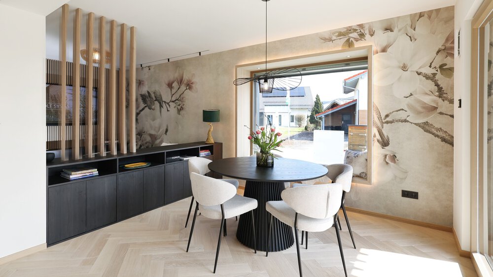 Modernes Esszimmer mit rundem schwarzen Tisch, vier weißen Stühlen, geblümter Tapete und großem Fenster.