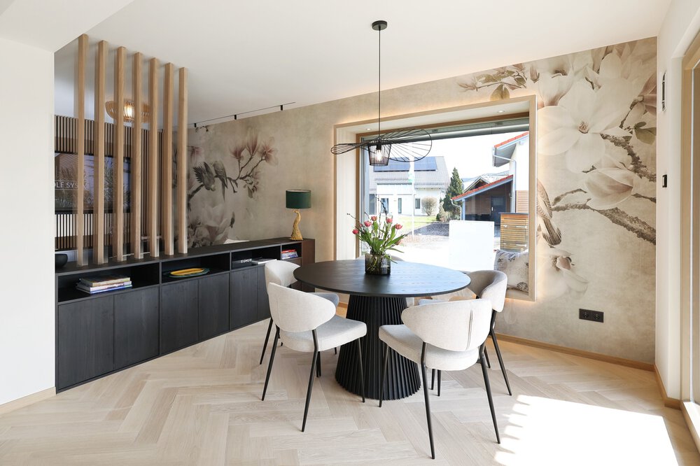 Modernes Esszimmer mit rundem schwarzen Tisch, vier weißen Stühlen, geblümter Tapete und großem Fenster.