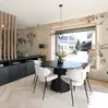 Modernes Esszimmer mit rundem schwarzen Tisch, vier weißen Stühlen, geblümter Tapete und großem Fenster.