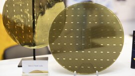 Nahaufnahmen zweier goldener Leiterplatinen in runder Form. Davor steht ein Schild mit der Bezeichnung „300mm FlexIC wafer“.