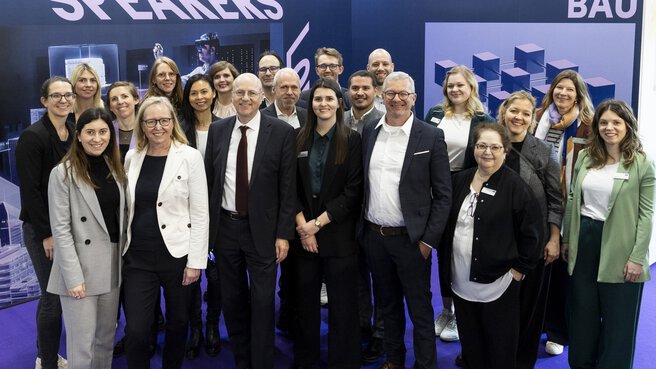 Sprecher auf der digitalBAU posieren als Gruppe auf einem violetten Teppich vor blau bedruckten Wänden mit digitalBAU Branding.