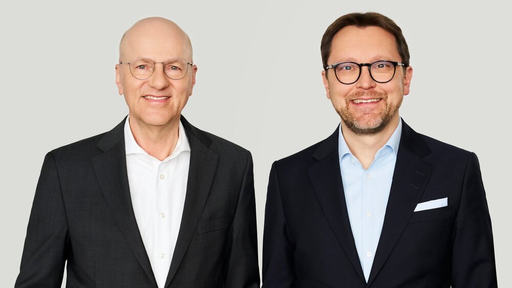 The photo shows two gentlemen, the CEOs of Messe München, both wearing black suits.