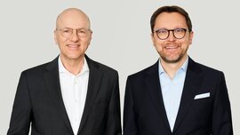 The photo shows two gentlemen, the CEOs of Messe München, both wearing black suits.