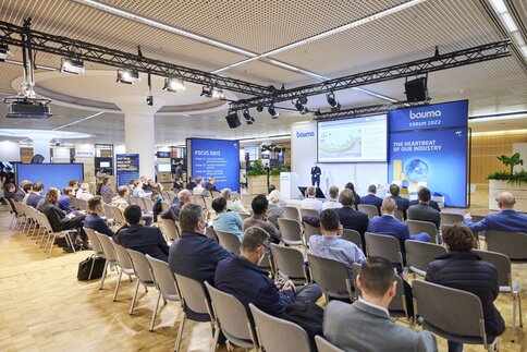 Group of people sitting in a room listening to a presentation at the Bauma Forum 2022.