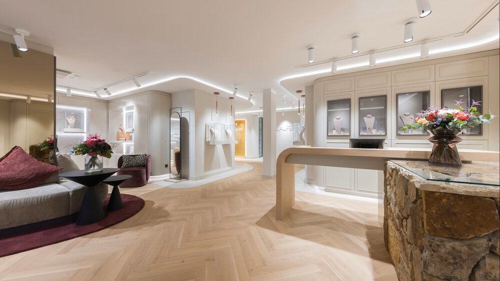 A large salesroom with rounded edges, seating, display cases for jewelry, and a sales counter that is partly made of stone.