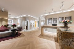 A large salesroom with rounded edges, seating, display cases for jewelry, and a sales counter that is partly made of stone.