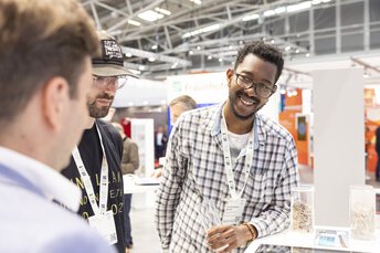Mehrere Personen stehen an einem Messestand und führen ein Gespräch in einer Ausstellungshalle.