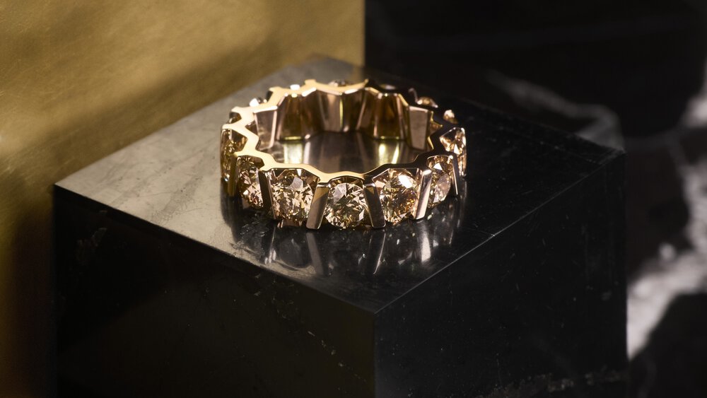 Gold ring with a geometric design on a dark marble surface.