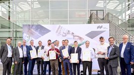 Eine Gruppe von Menschen posiert mit Auszeichnungen vor einer Messehalle und einem Plakat der World of Photonics.