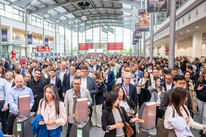 A large crowd waits in the West Entrance Hall to enter the Transport Logistic 2025 exhibition halls at the turnstiles.