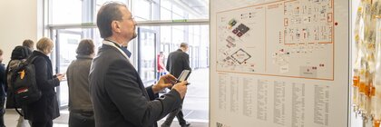 A man looks at the LOPEC overview map at the entrance to the trade fair, people walk past in the background.