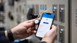 Zwei Hände halten in der linken Hand einen Schlüssel und in der Rechten Hand ein Smartphone. Auf dem Smartphone ist eine Sicherheitssoftware zu sehen, die den Schlüssel erkennt.