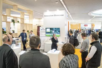 People gathered around a presentation at a stand labeled “Innovation Showcase” with displays and screens.