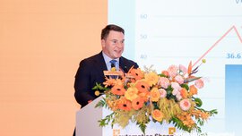 Man giving a presentation at a podium at automatica Shanghai with a slide and floral arrangement in front.