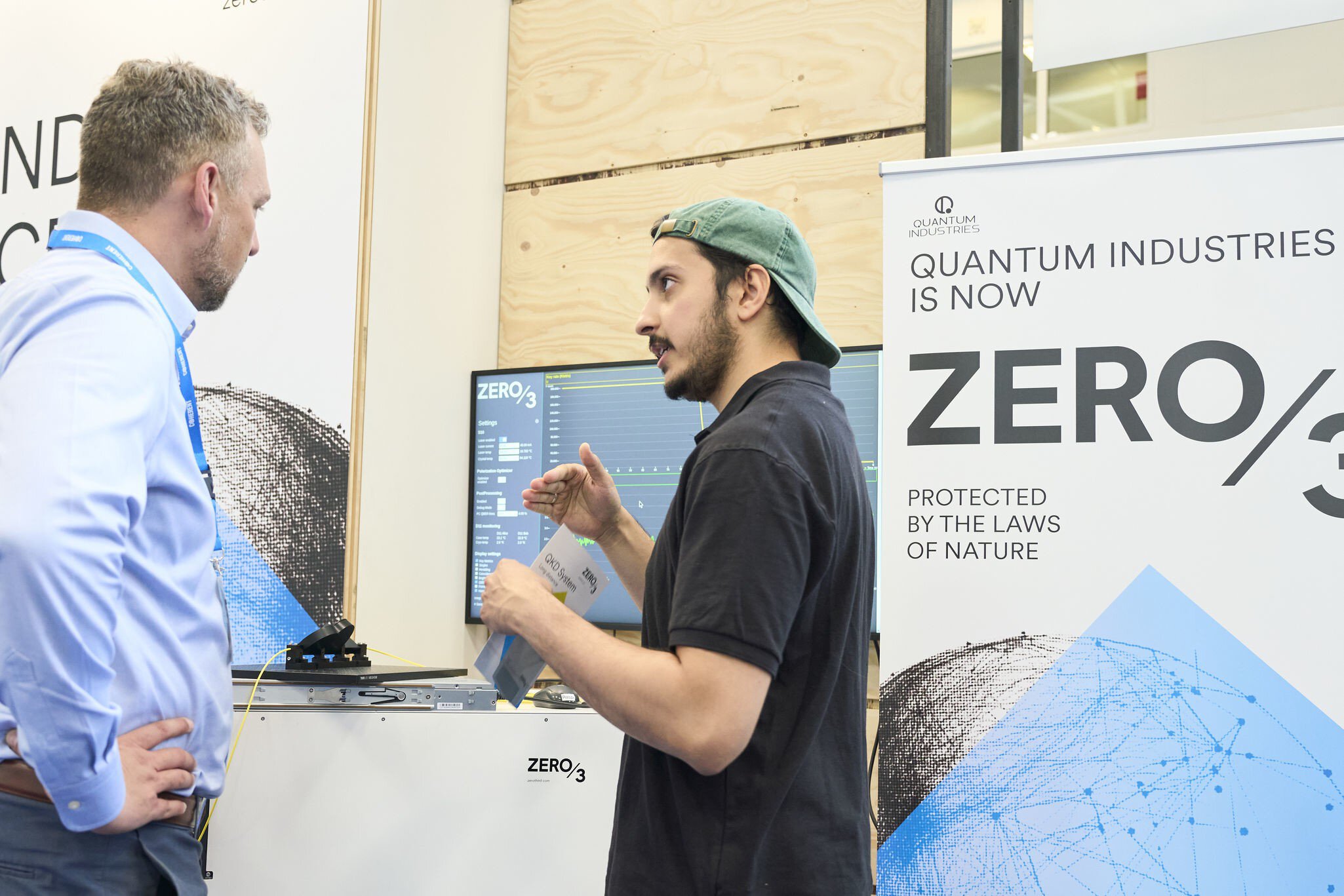 Zwei Personen im Gespräch an einem Messestand der World of Quantum vor einer Präsentation zur Quantenkommunikation.