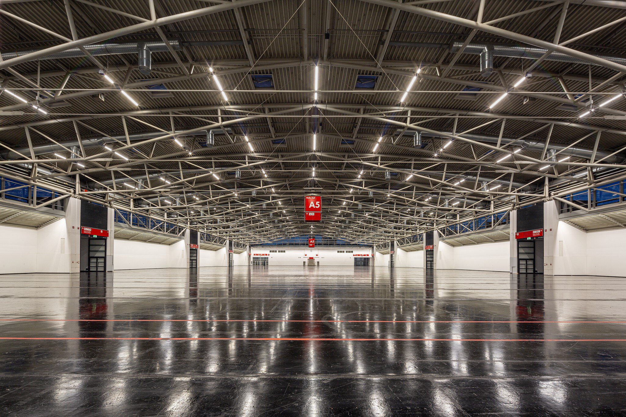 Geräumige, leere Industriehalle mit Metalldeckenbalken, poliertem dunklem Boden und roten A5-Schildern darüber