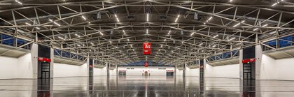 A spacious, empty industrial hall with exposed metal beams, a polished dark floor and red A5 signs hanging above.