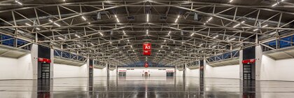 Geräumige, leere Industriehalle mit Metalldeckenbalken, poliertem dunklem Boden und roten A5-Schildern darüber