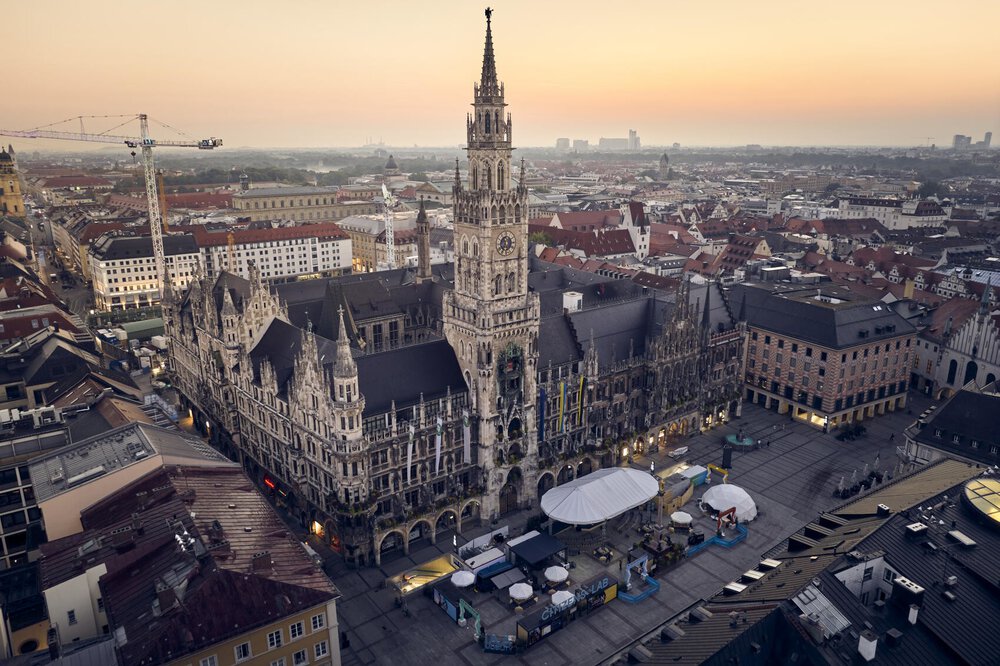 Luftaufnahme des Neuen Rathauses in München bei Sonnenuntergang, umgeben von städtischen Gebäuden und einem offenen Platz.